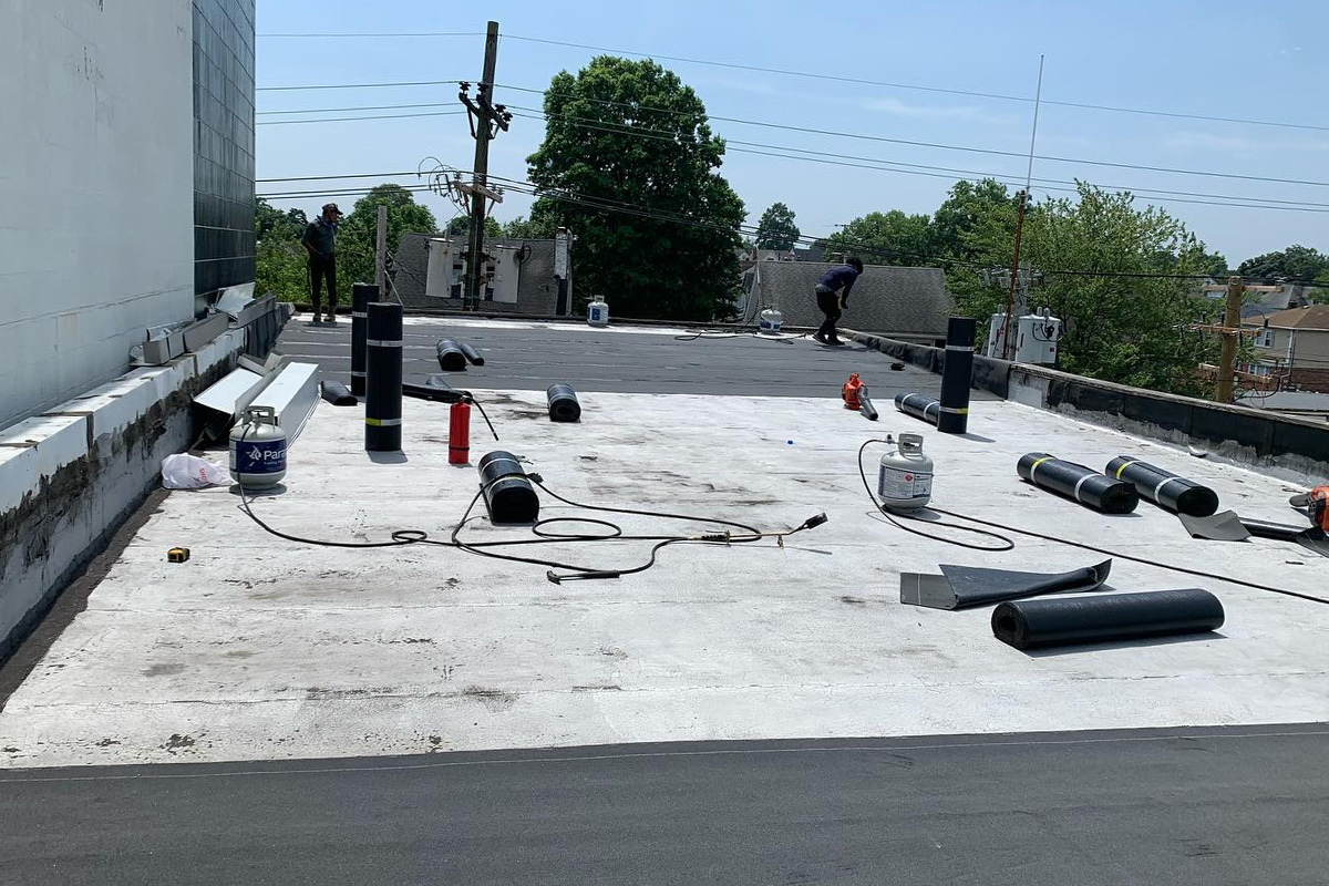 Workers use torches for roof repair to seal flat commercial roofs, while residential projects involve installing dark asphalt shingles over protective layers.