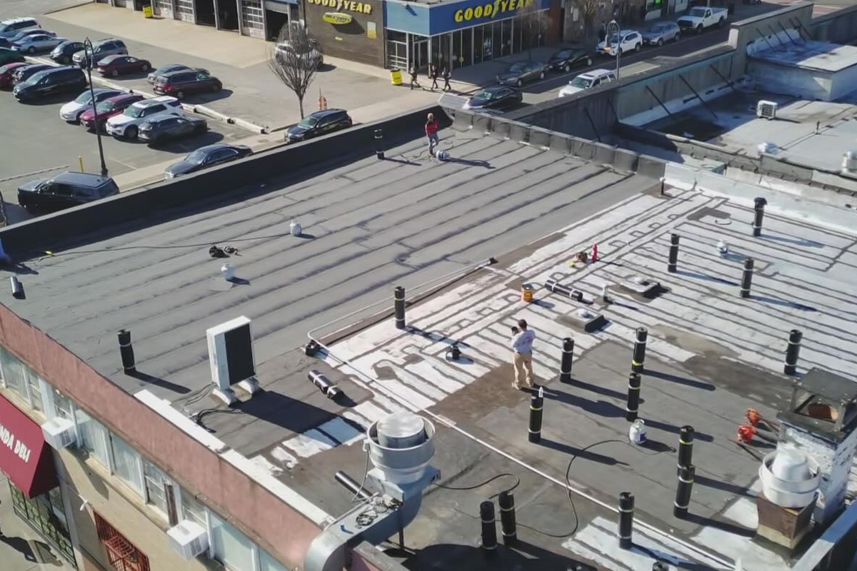 Workers repair a large commercial flat roof with visible vents, while residential projects feature grey shingle installation and ZIP System weatherproofing.