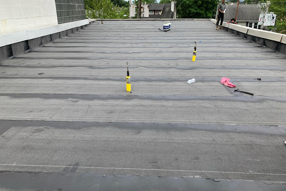 Roofers use propane torches and rolls of membrane to repair large commercial flat roofs. Residential work includes maintaining dark asphalt shingles on sloped roof sections.