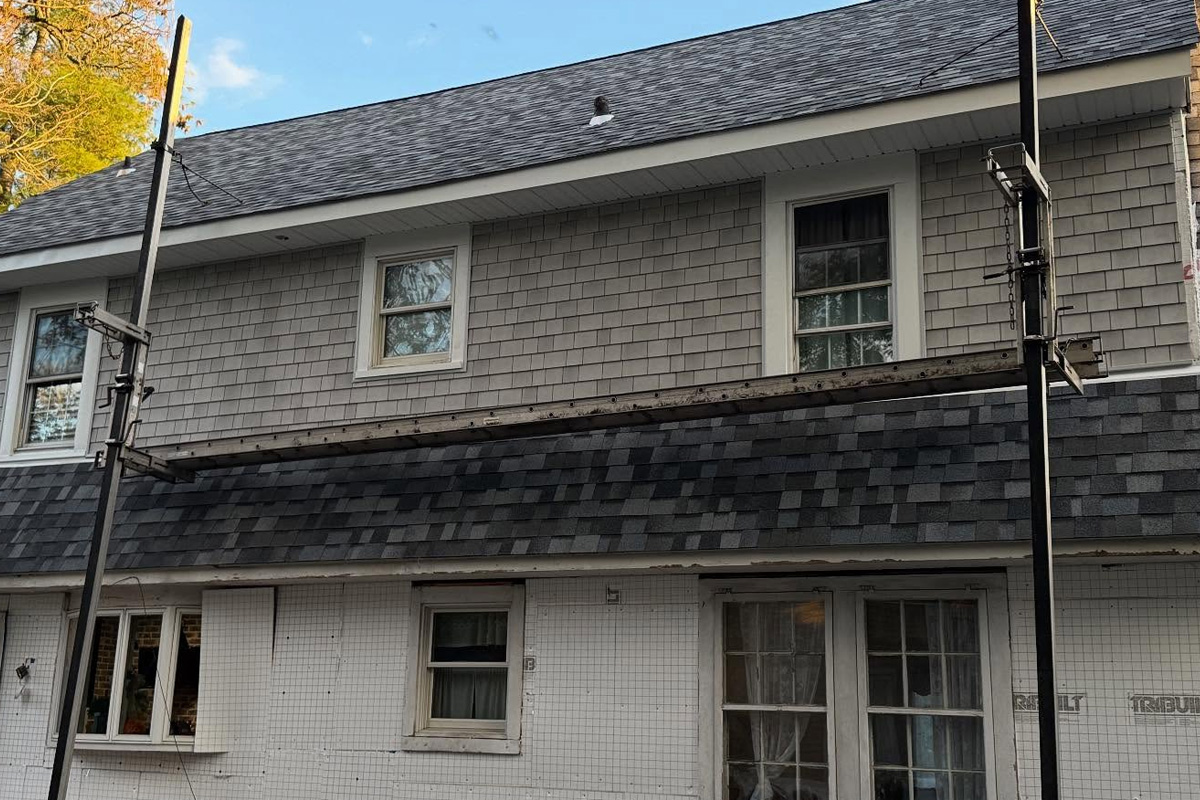 Installation of textured grey shingle siding is shown on the upper story of a residence in Long Island.