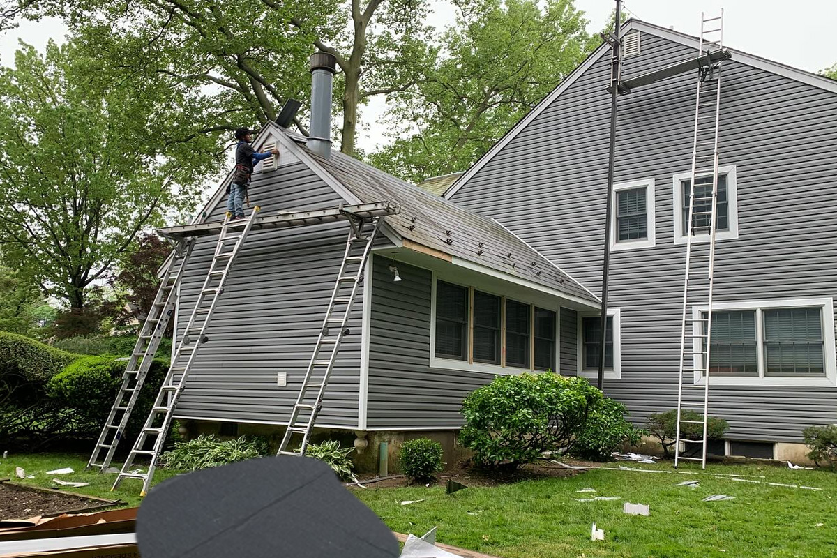 Gemini ha dicho Exterior siding materials include dark grey horizontal planks, textured grey shingles being installed near chimneys, and protective orange or green ZIP System sheathing in Long Island.