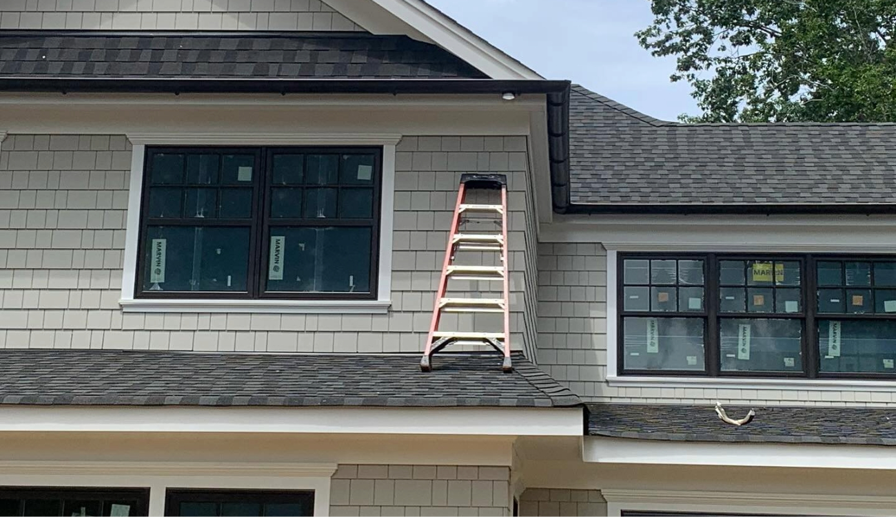 Professional roofing contractors at a residential job site using high ladders to perform a necessary soffit repair.