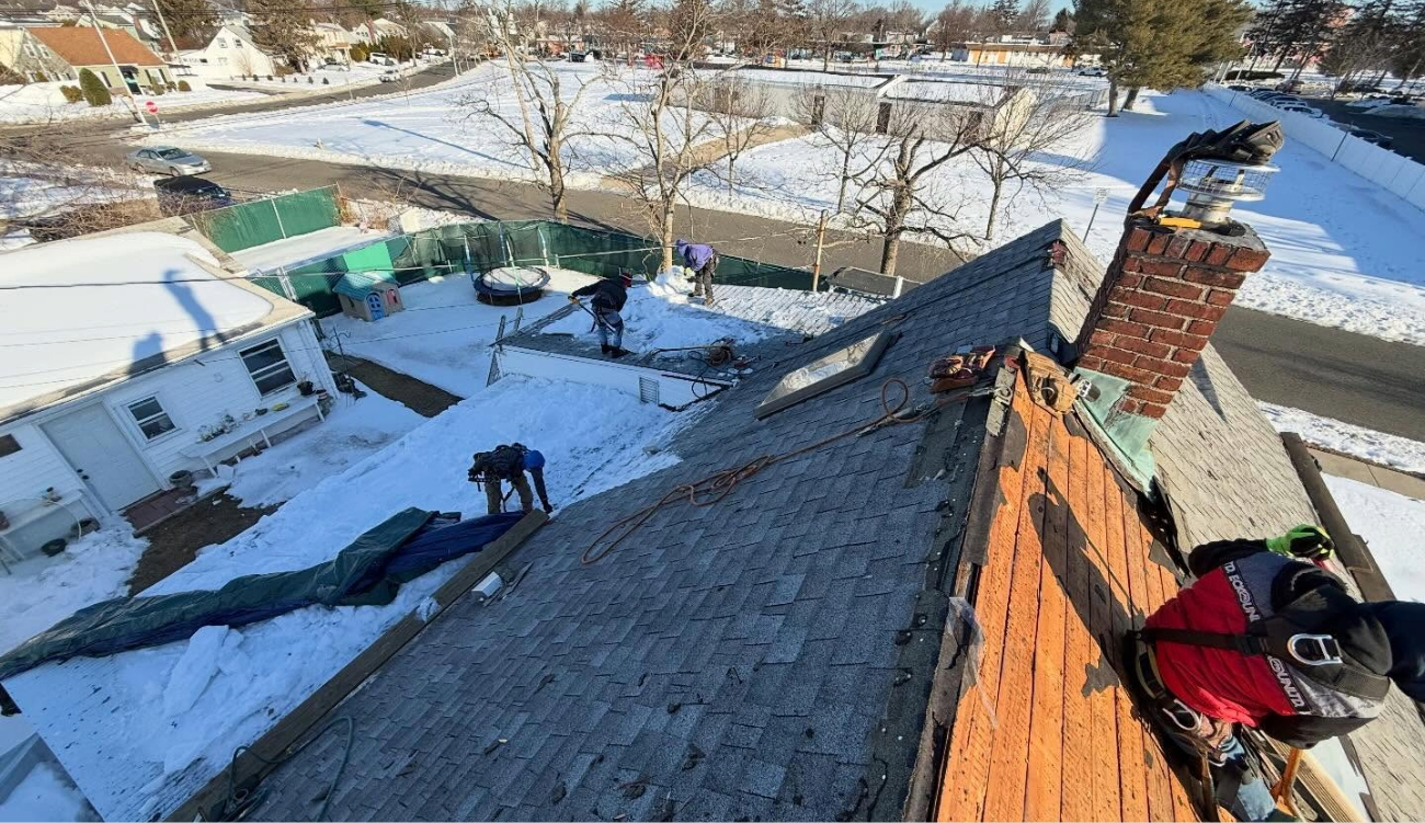 Roofers working on a snow-covered roof around a brick chimney during a flashing repair.