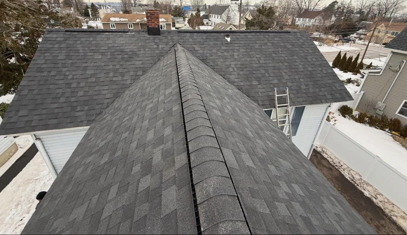 A high-angle view along a roof ridge vent on a winter day, demonstrating the durability and layout of different types of roofing shingles.