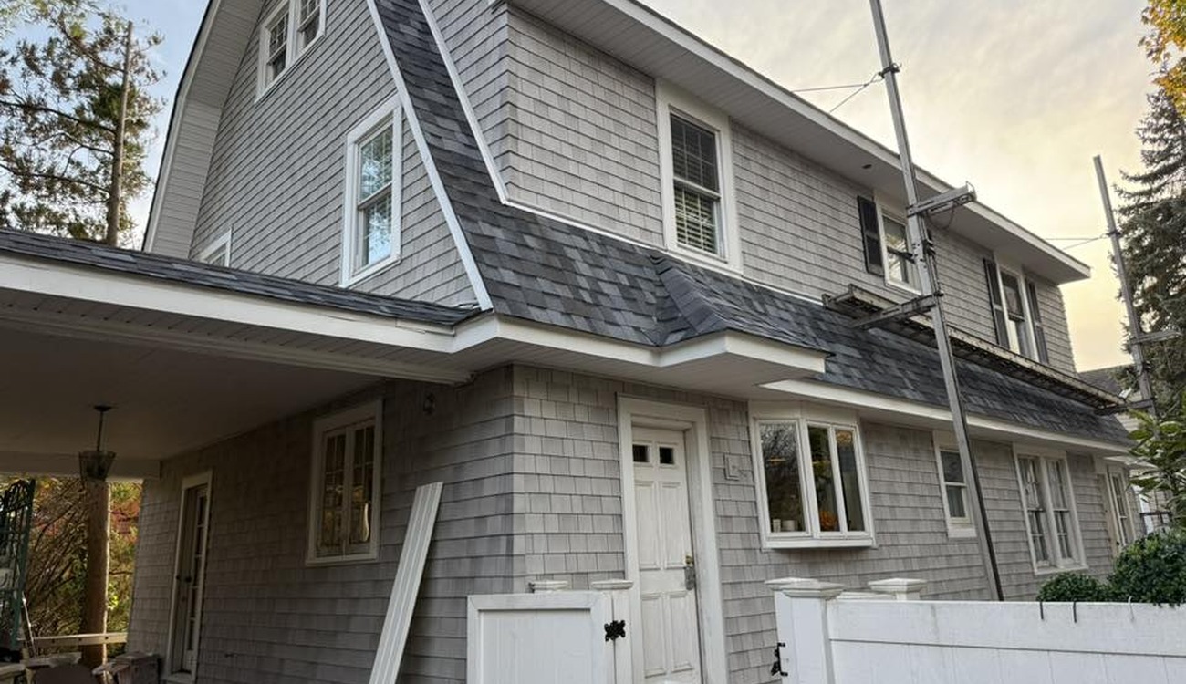 A tall grey shingled house receiving new dark roofing materials illustrates the typical roof replacement cost nassau county residents experience.