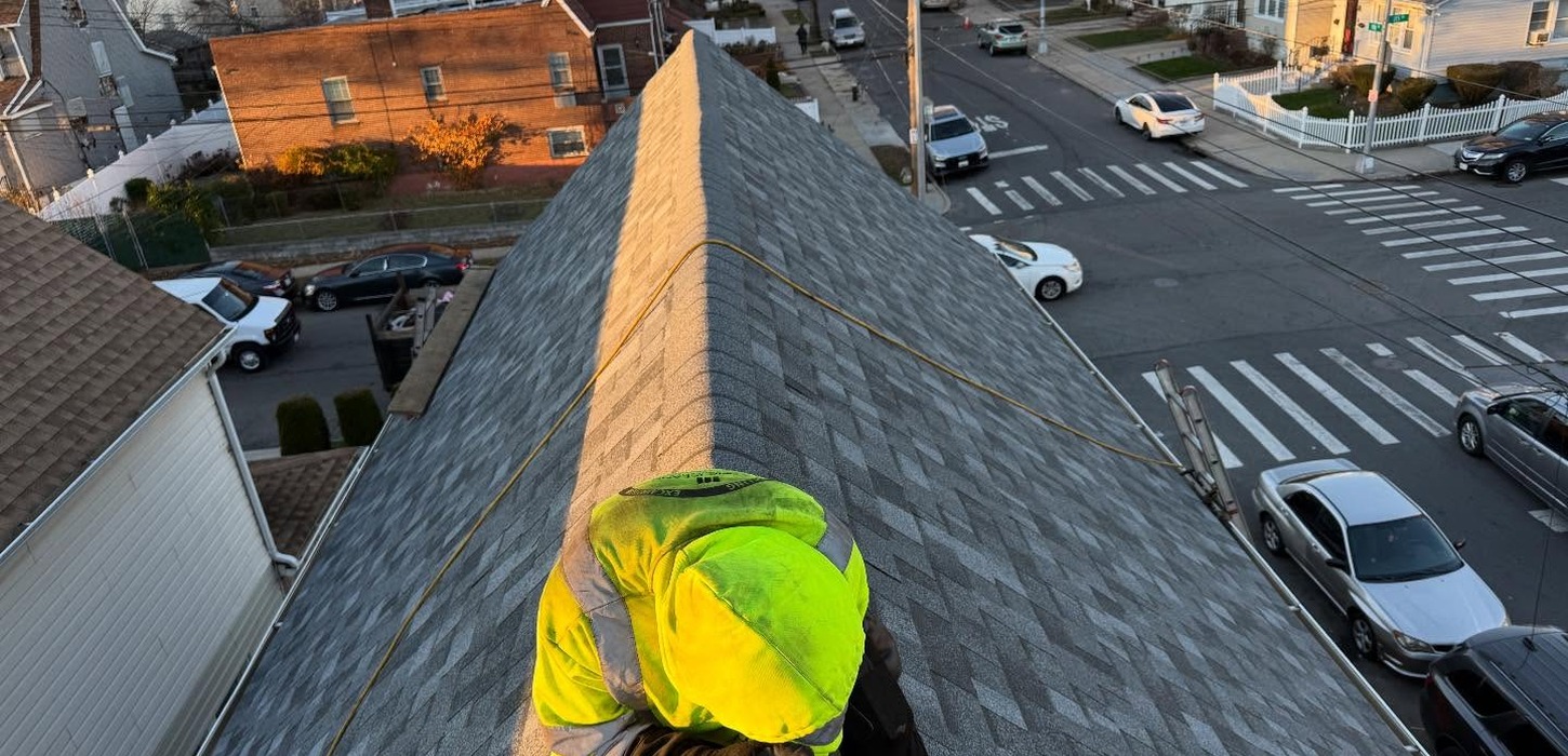 A worker in bright safety gear straddles a roof ridge, making homeowners wonder exactly how long does roof replacement take.