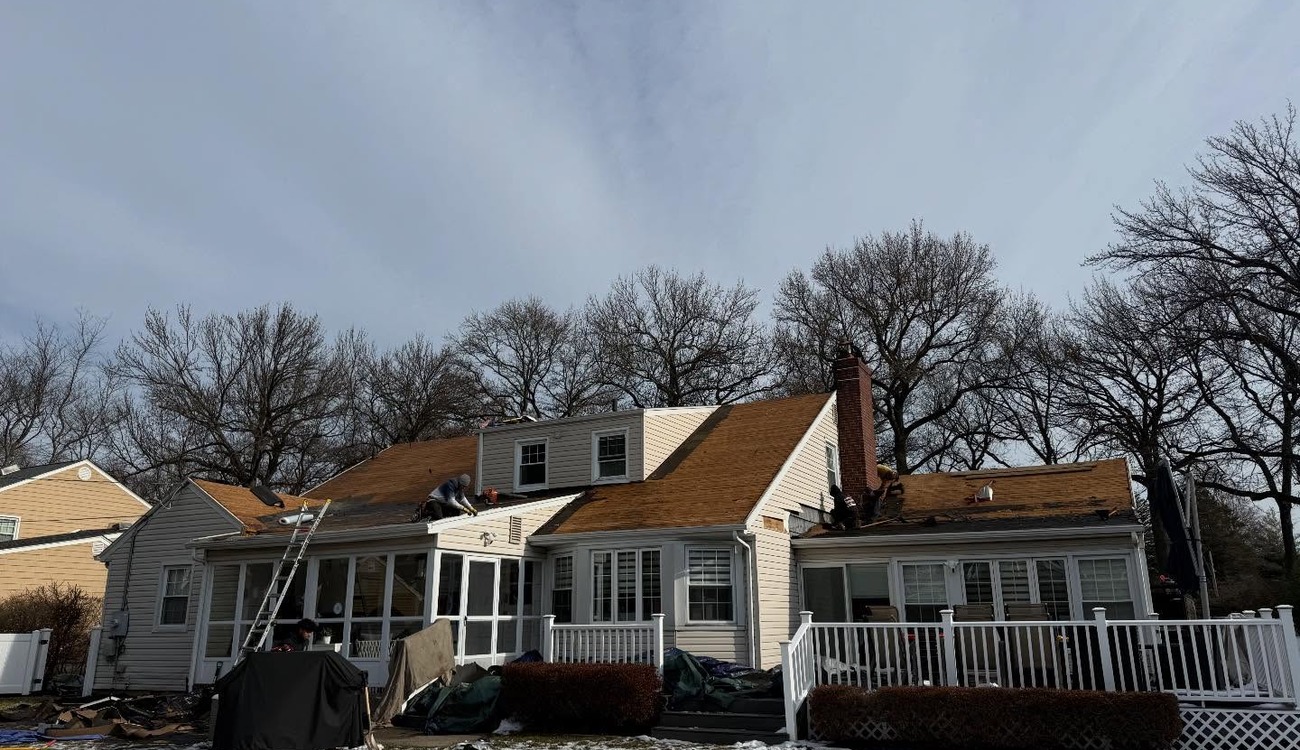 Roofers removing old brown shingles from a white home during winter proves just how long does roof replacement take sometimes.