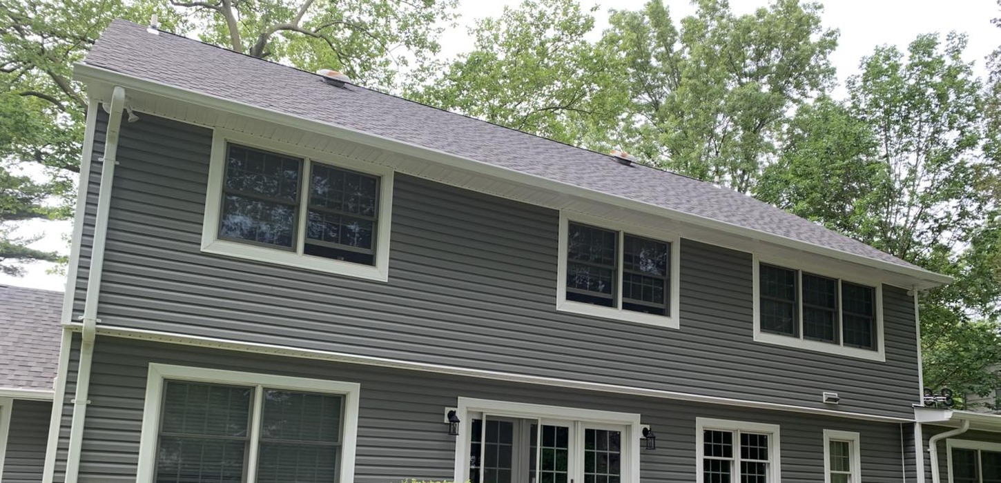 The clean backside view of a gray-siding home after a successful roof replacement in Long Island.